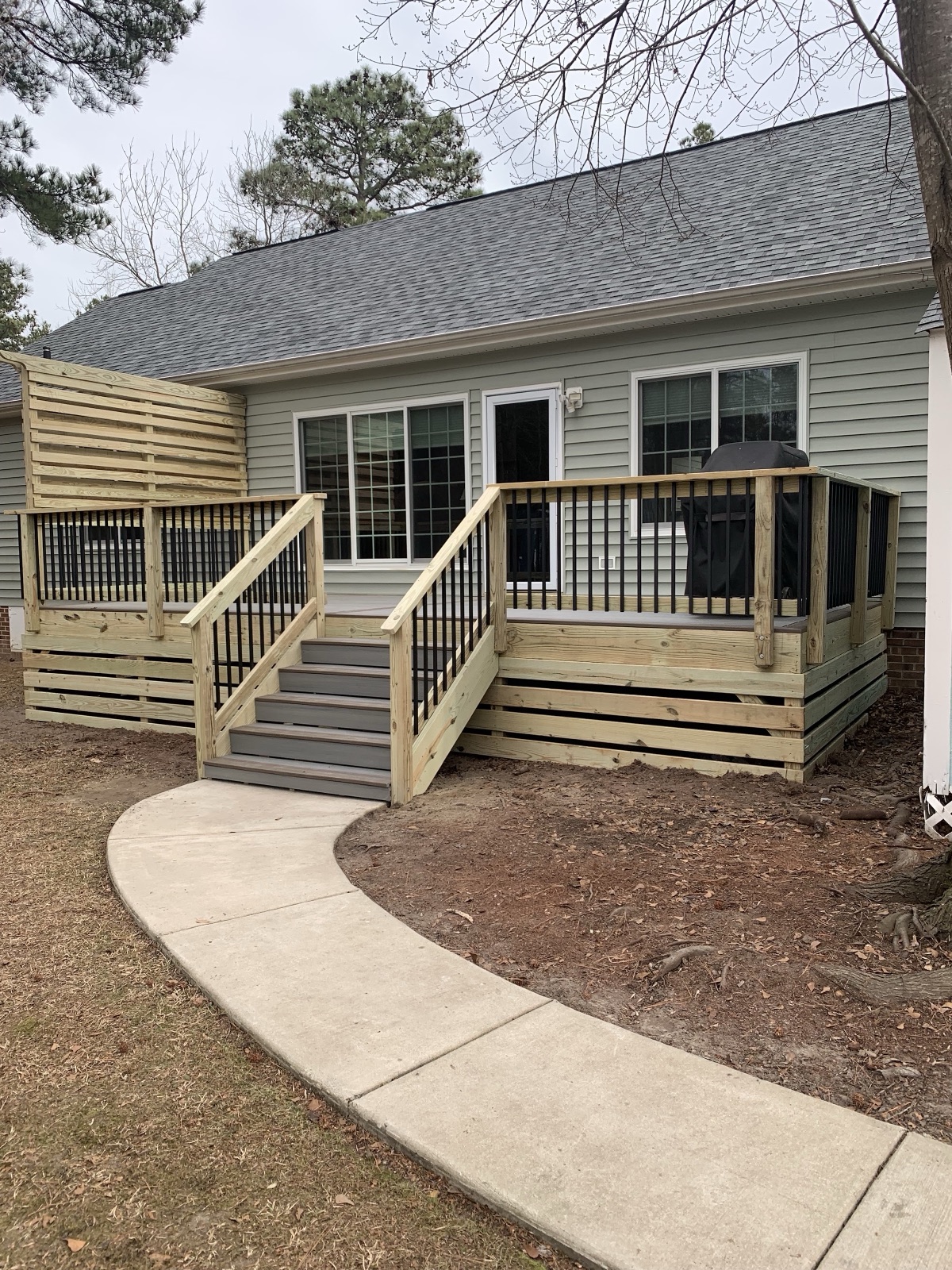 A pressure-treated deck with a horizontal privacy screen and a gentle access ramp, tied into a fresh concrete walkway.