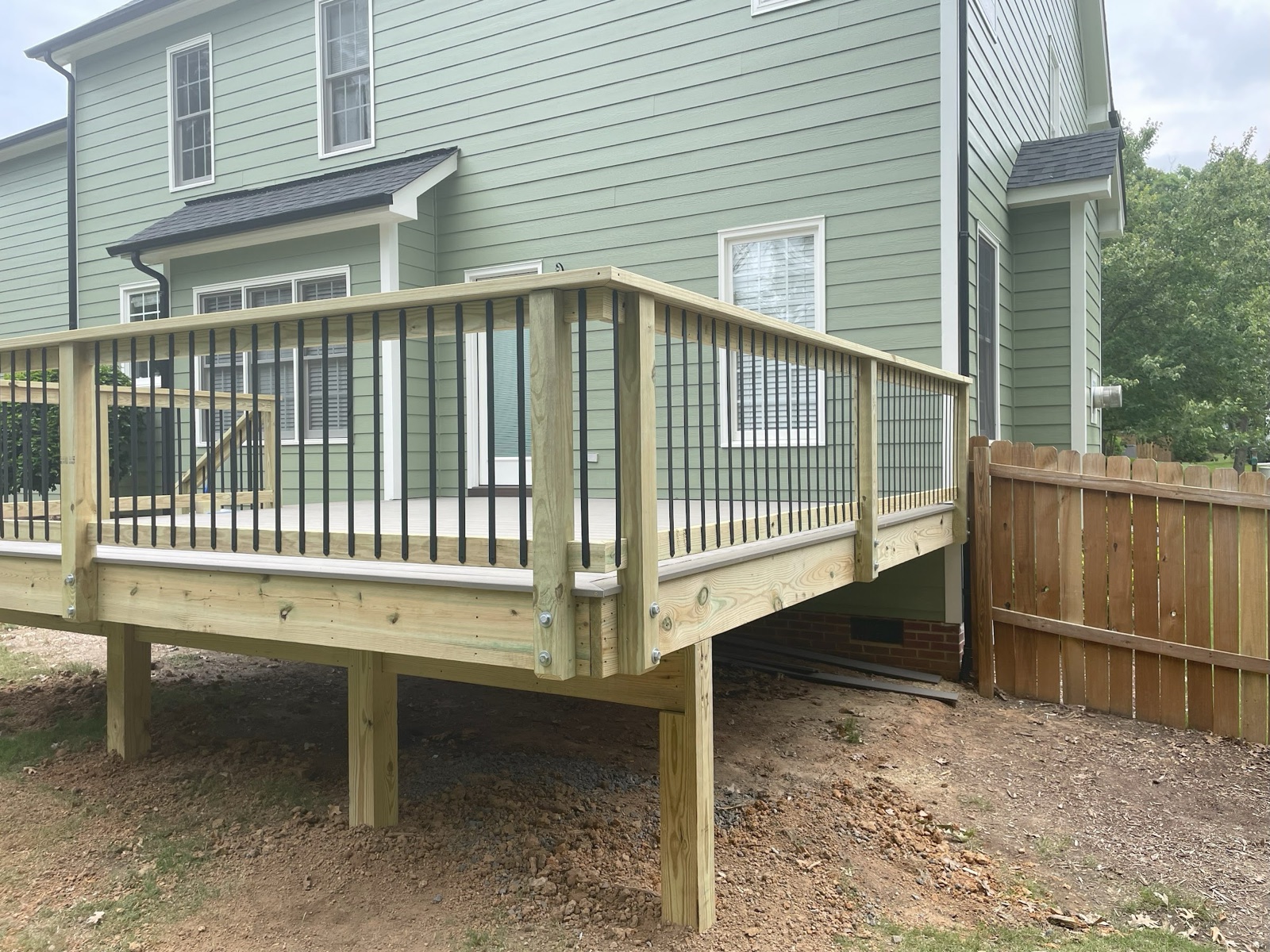 An elevated pressure-treated deck with black metal balusters, framed to sit level over sloping ground.