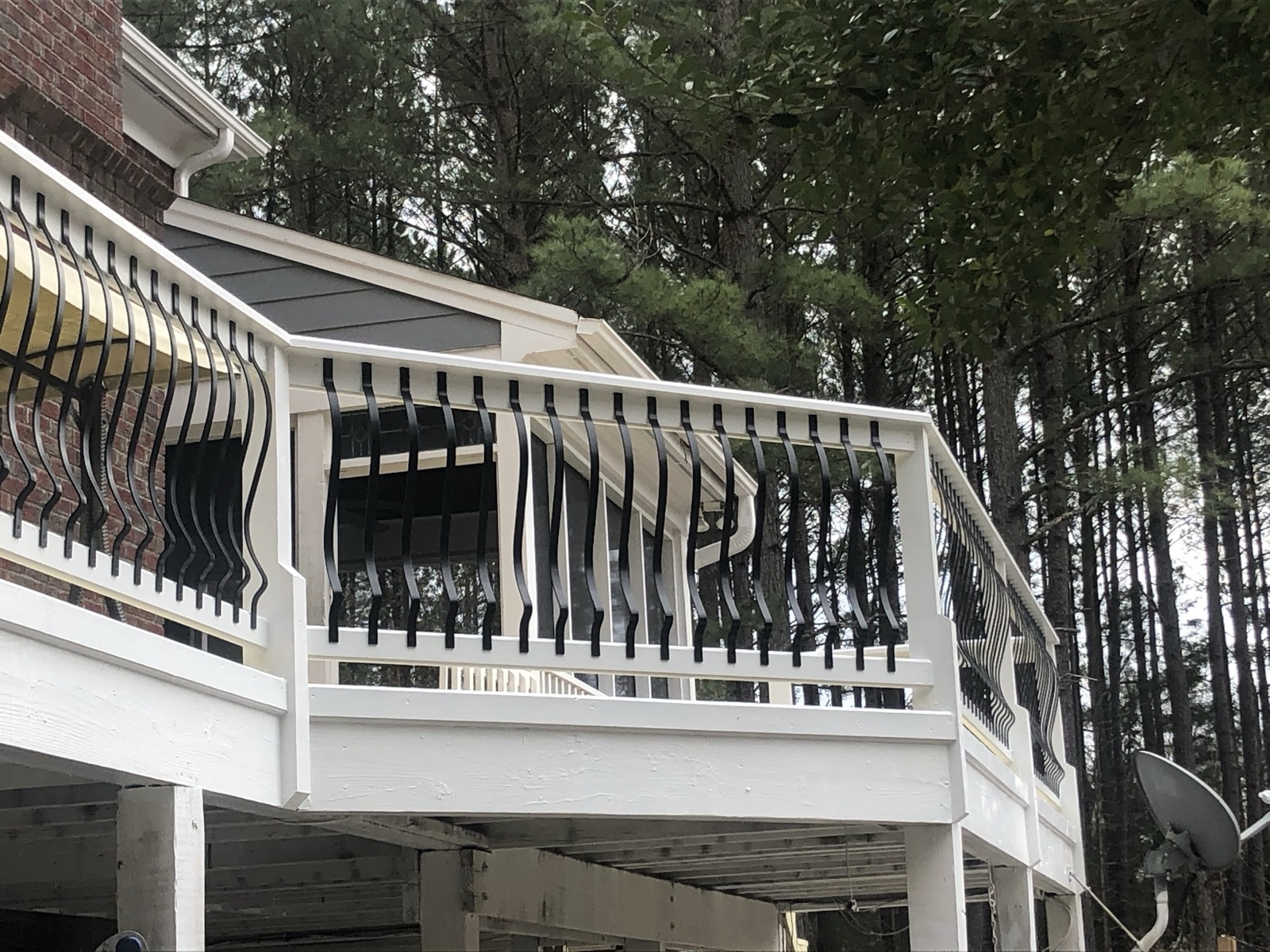 The rail line on an elevated deck, run clean and straight in white with black metal pickets against the tree line.